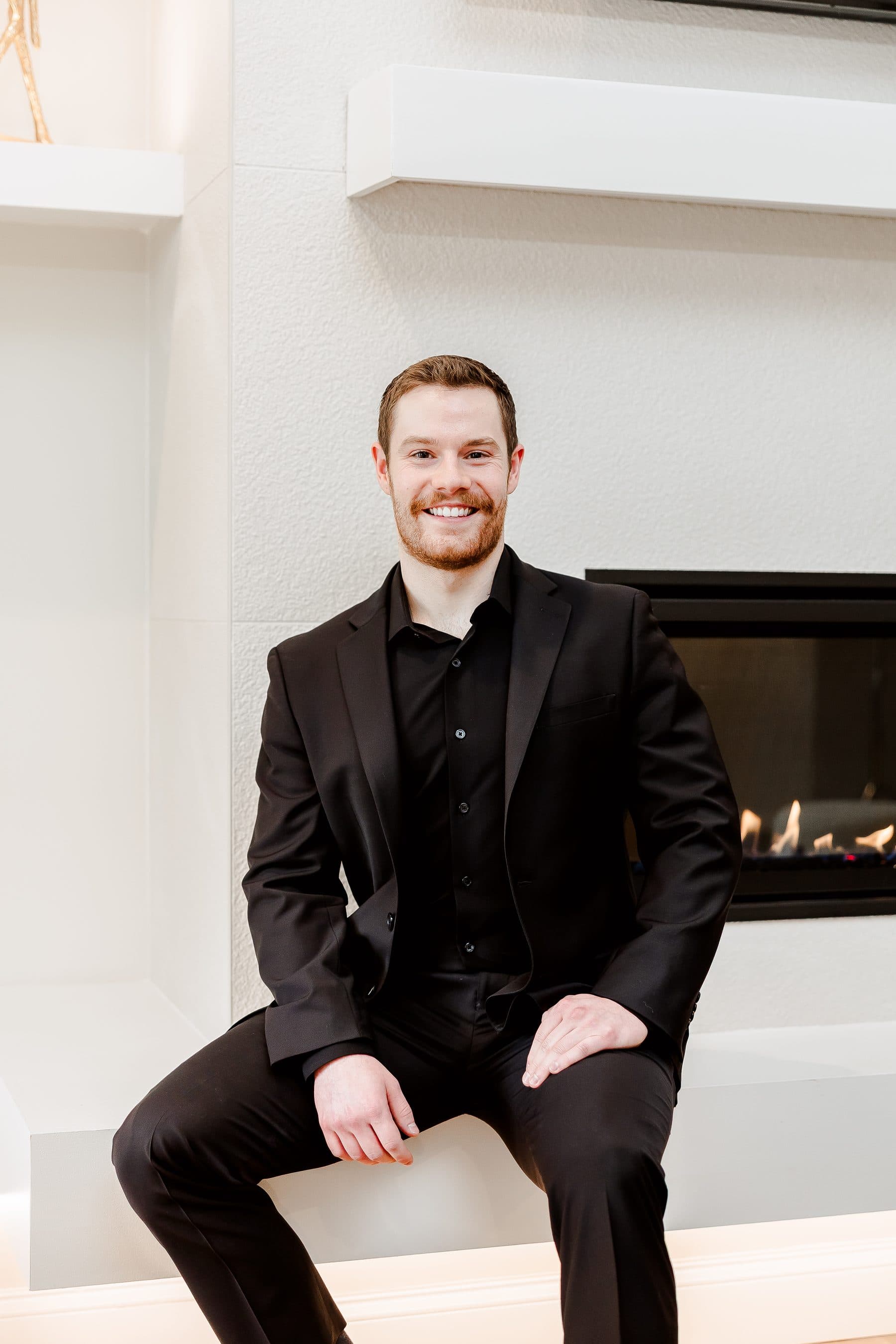 Jacob Peistrup seated on a fireplace hearth in a dark suit